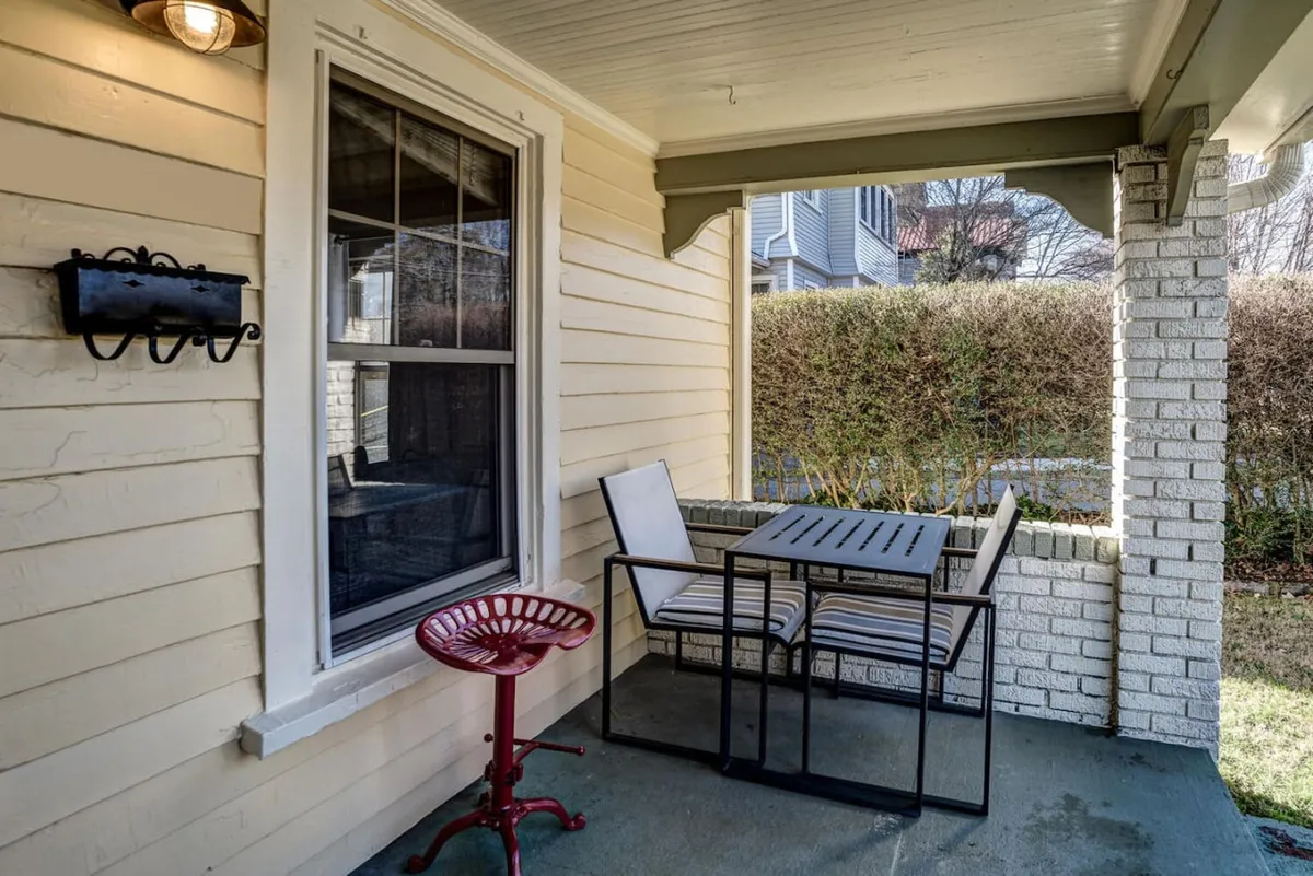 This image features a cozy exterior patio space with a red bar stool and a small dining table positioned near a window, inviting you to enjoy the fresh air. The scene is bathed in soft, natural light, suggesting sunrise or early morning, and hints at a relaxed atmosphere ideal for enjoying coffee, reading, or casual dining.
