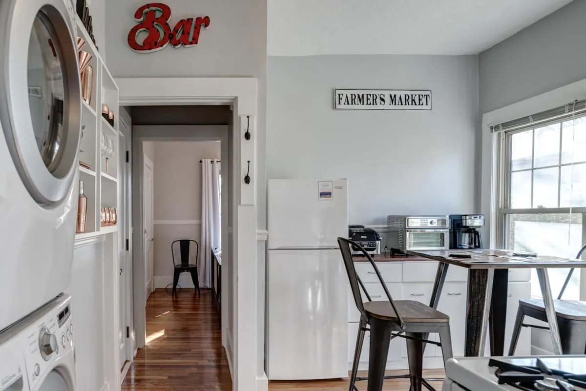 This image captures a cozy interior space featuring a dining table, kitchen appliances, and decorative signs ('Bar' and 'Farmer's Market'). The scene exudes a welcoming atmosphere for both cooking and dining, with a nod to local flavors and the social aspects of sharing meals. Appliances and signs hint at both everyday convenience and the charm of exploring local produce.